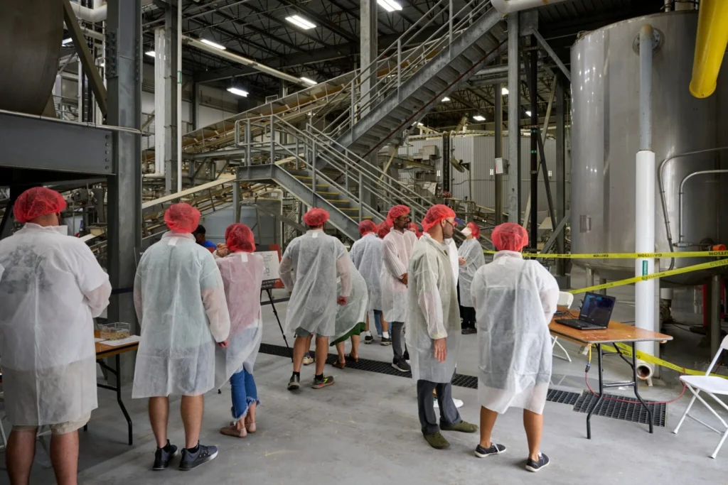 People in white lab coats and hair nets tour a soy sauce factory 